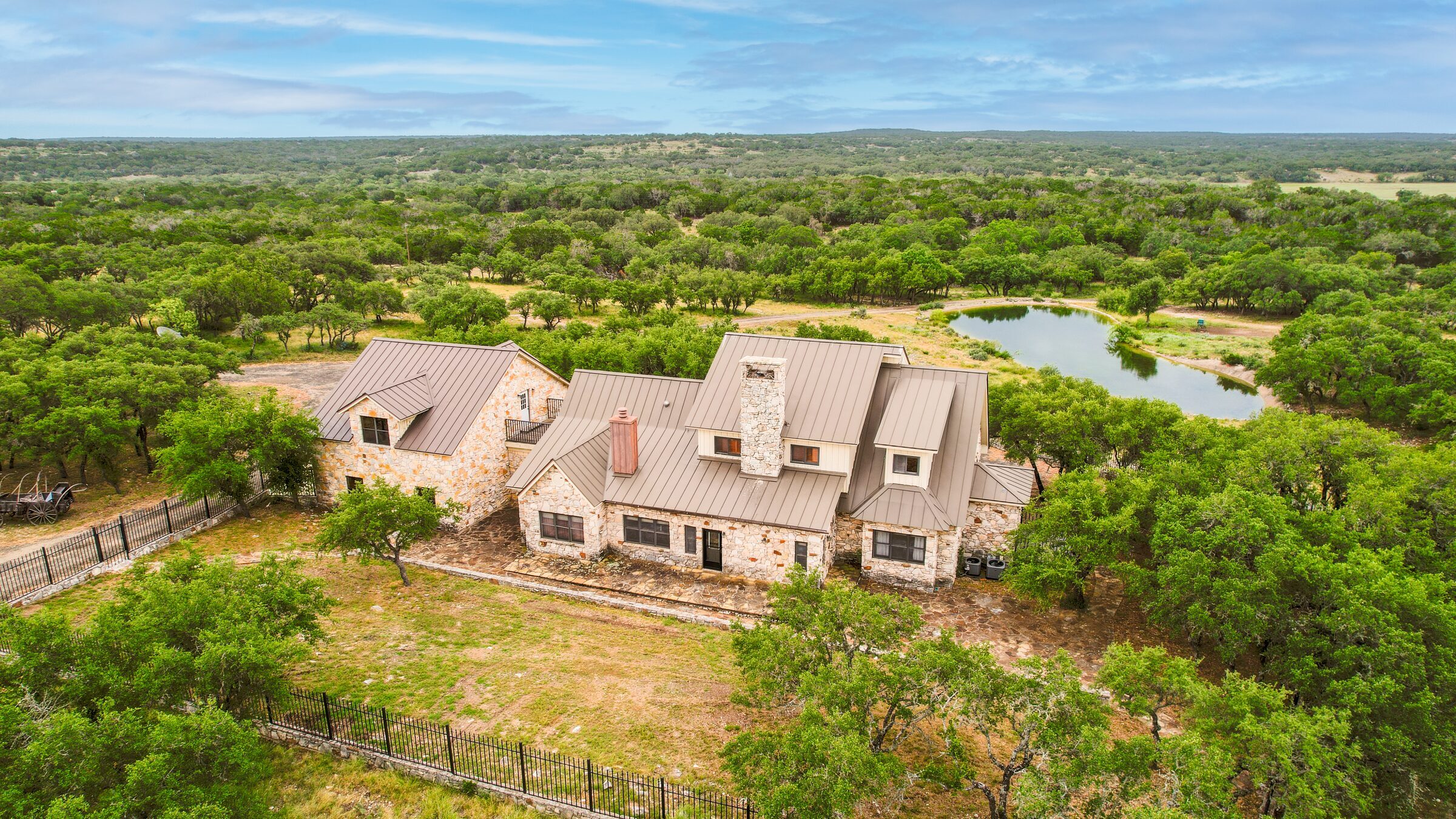 Aerial view of the rock lodge at 1305 NW Camino Real, Mountain Home Texas, with the stocked pond and surrounding oak cover