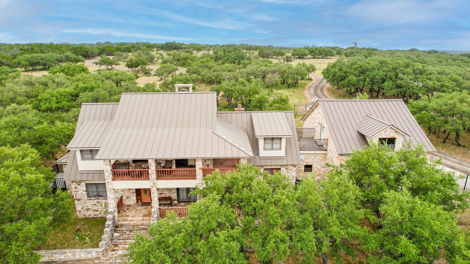 Aerial view of the main lodge, porches and metal roofs set among oaks with the ranch road behind