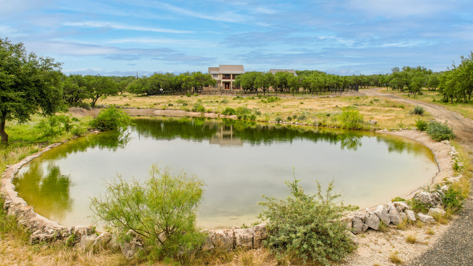 The concrete-lined stocked pond seen from the bank, with the lodge and guest cabin on the rise behind it