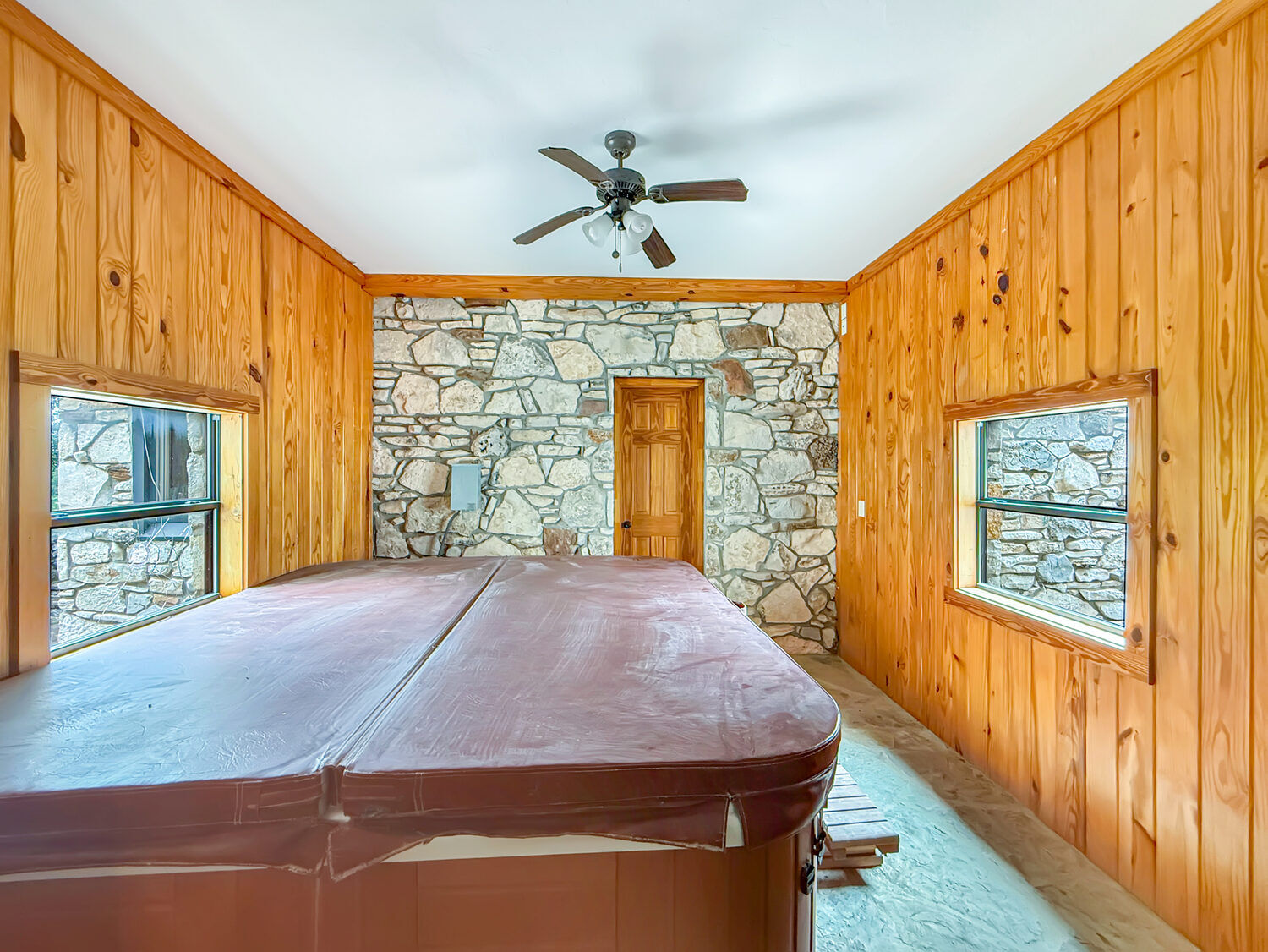 Indoor hot tub room finished in knotty pine with a stone accent wall and windows on two sides