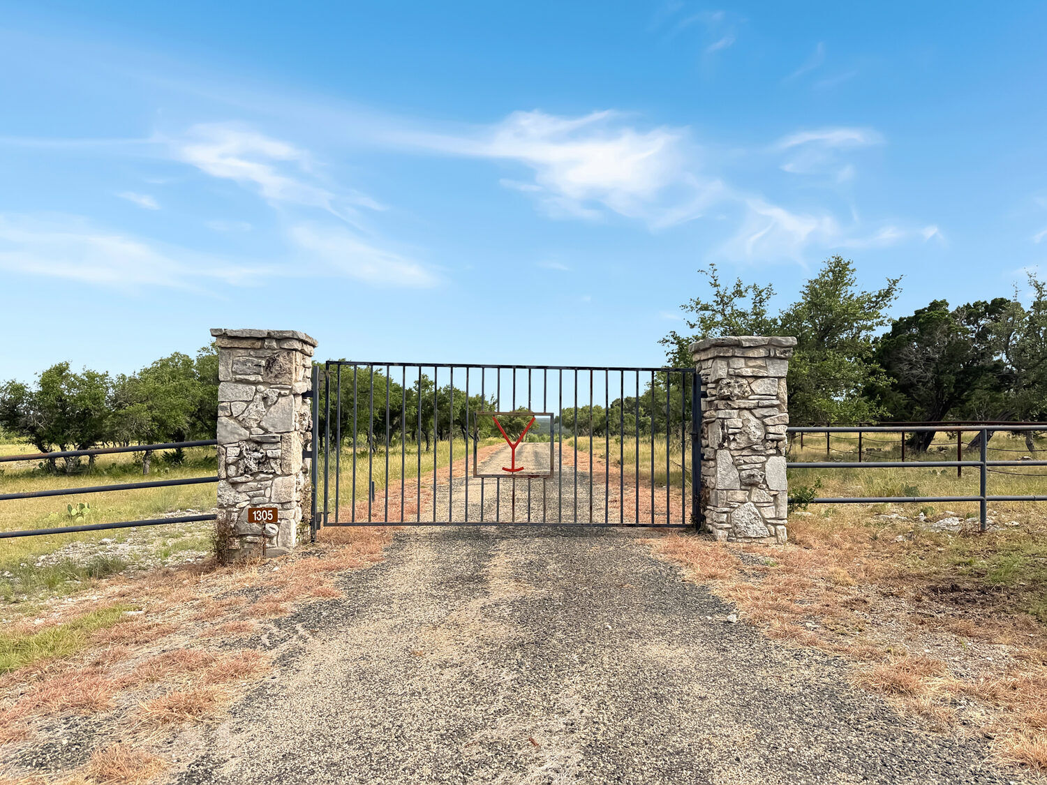 Stone-pillar entrance gate at 1305 NW Camino Real with the caliche drive running back into the oaks
