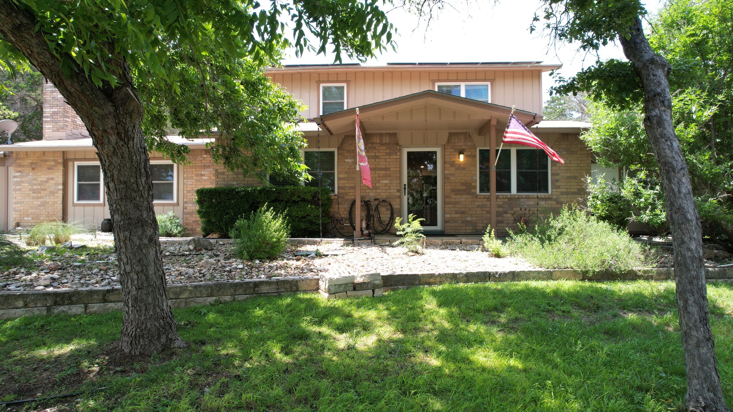 Front elevation of the house — brick with a covered entry, shaded by mature trees, with a lawn in front