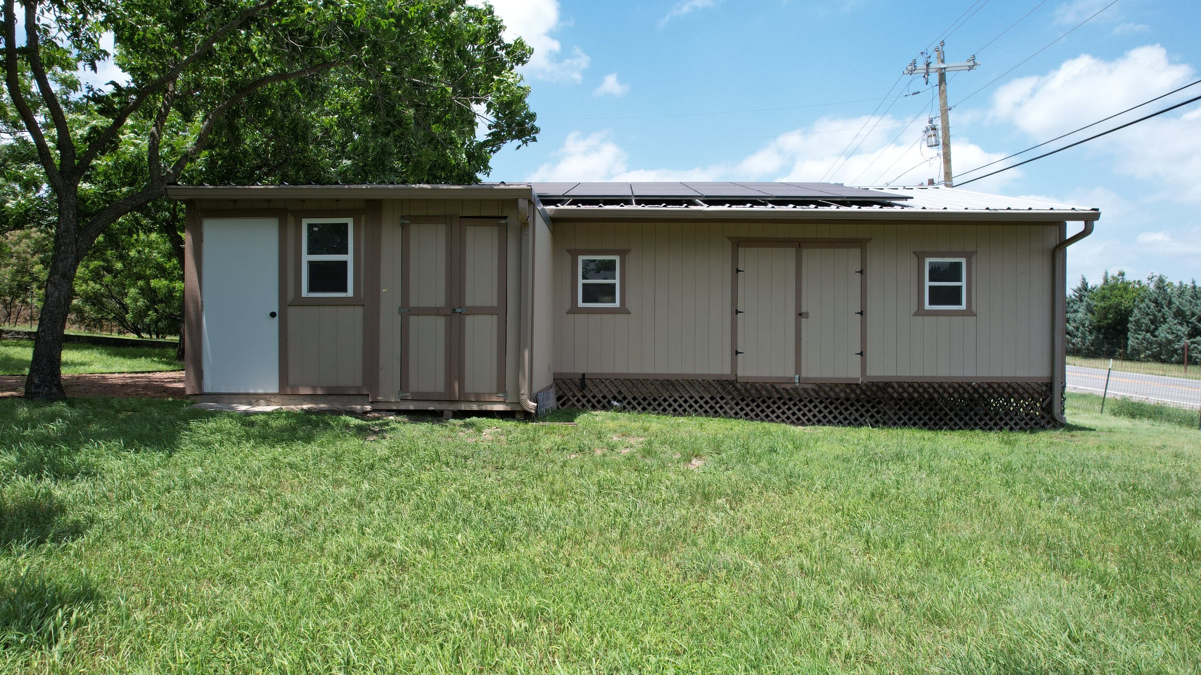 The outbuilding with an attached storage room, its metal roof carrying rail-mounted solar panels