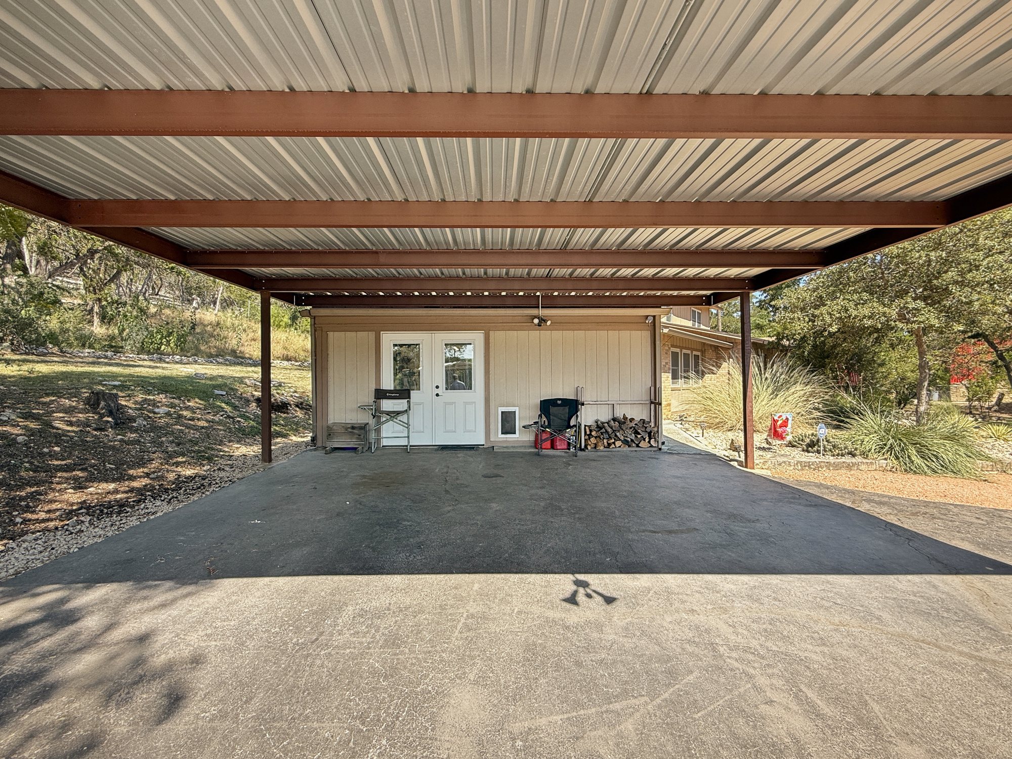 Covered parking on a concrete slab under a tall metal roof, with double doors into a storage room at the back