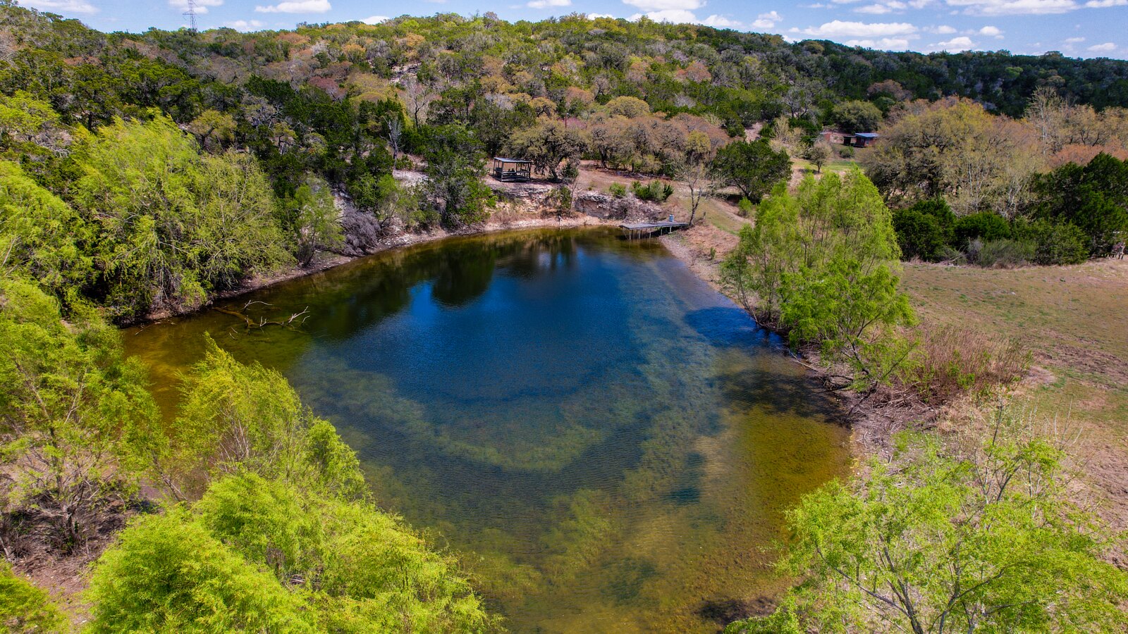 The spring-fed pond at 150 Coker Hollow seen from the air, with the dock on the far bank and the wooded canyon walls around it