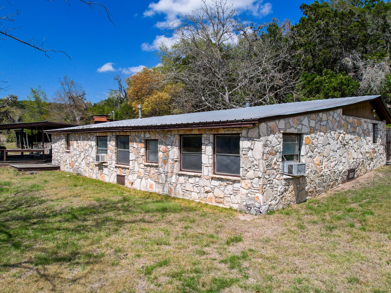 The native rock ranch house at 150 Coker Hollow from the yard, one story with a metal roof and window air conditioning units