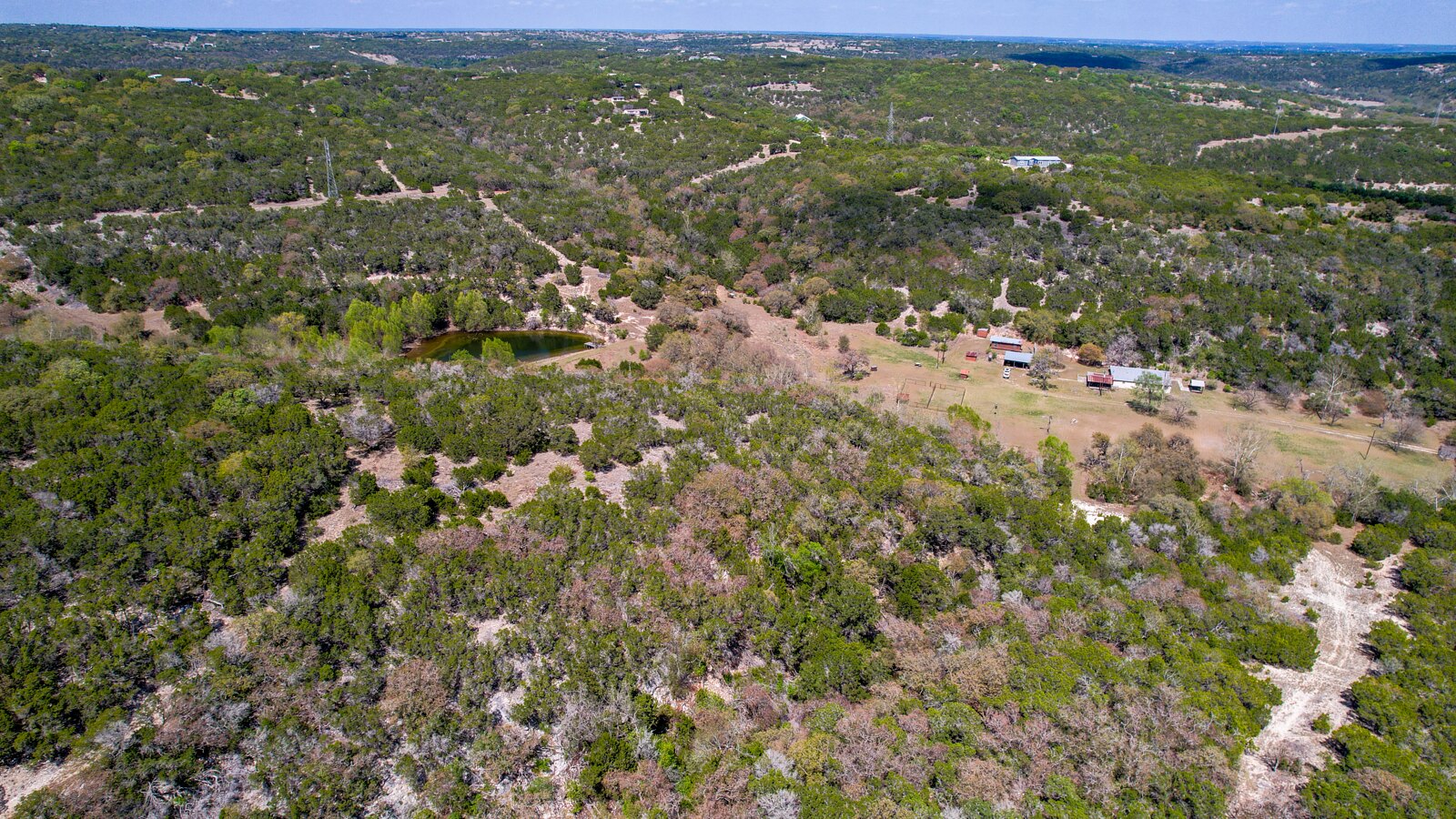 High aerial over 150 Coker Hollow showing the pond, the homestead flat and the wooded hill country running out to the horizon