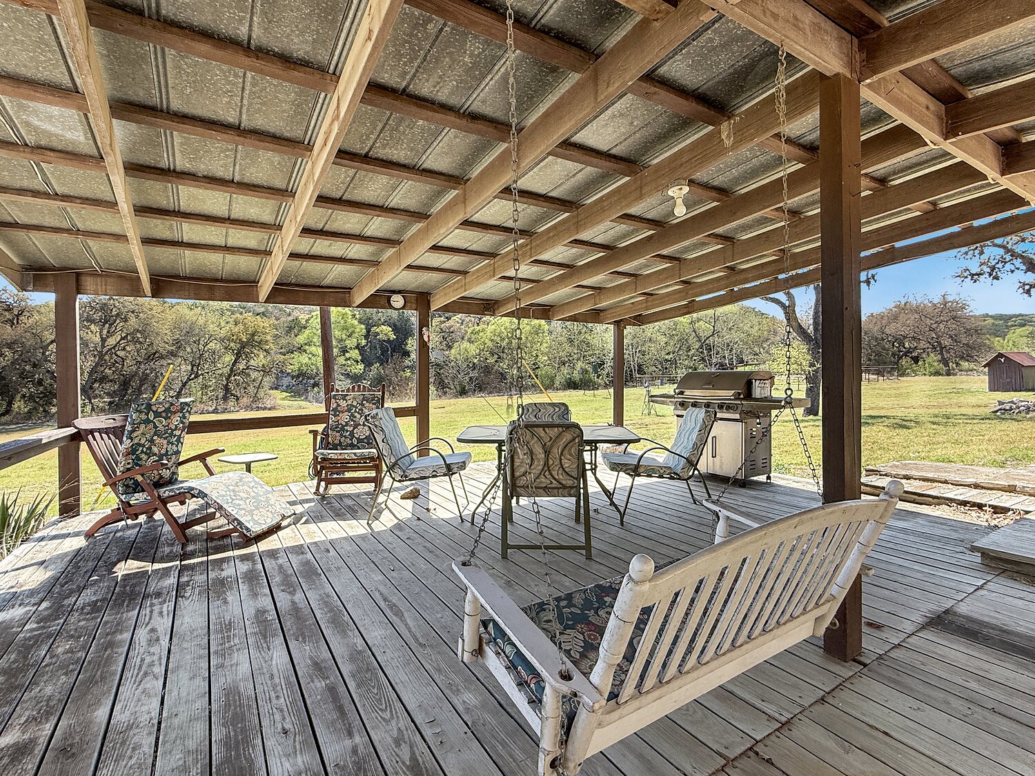 The covered porch at 150 Coker Hollow with a swing, chairs and a table, looking out across the meadow to the hills