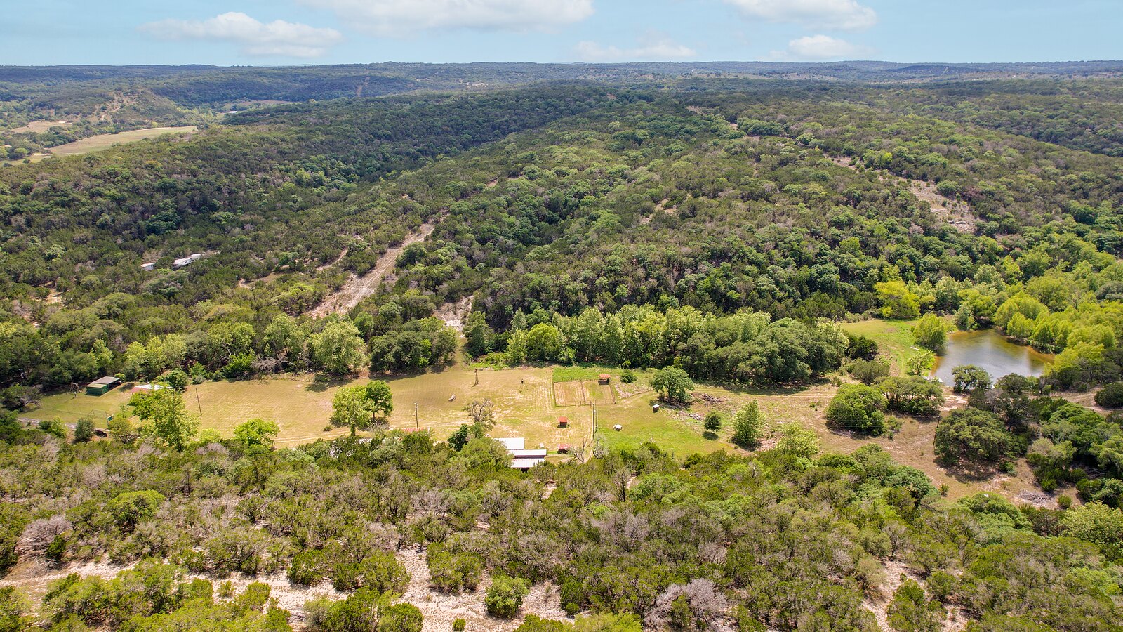 Wide aerial across the box canyon at 150 Coker Hollow with the meadow, the buildings and the pond set among wooded hillsides