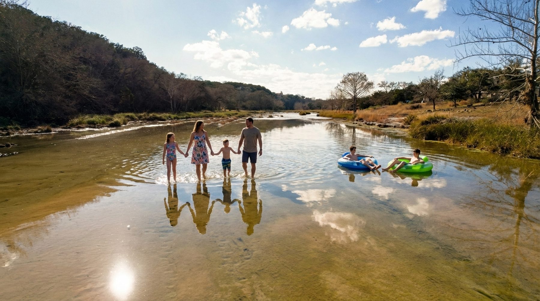 Composite image of a family wading in shallow river water with two people on inner tubes under a blue sky