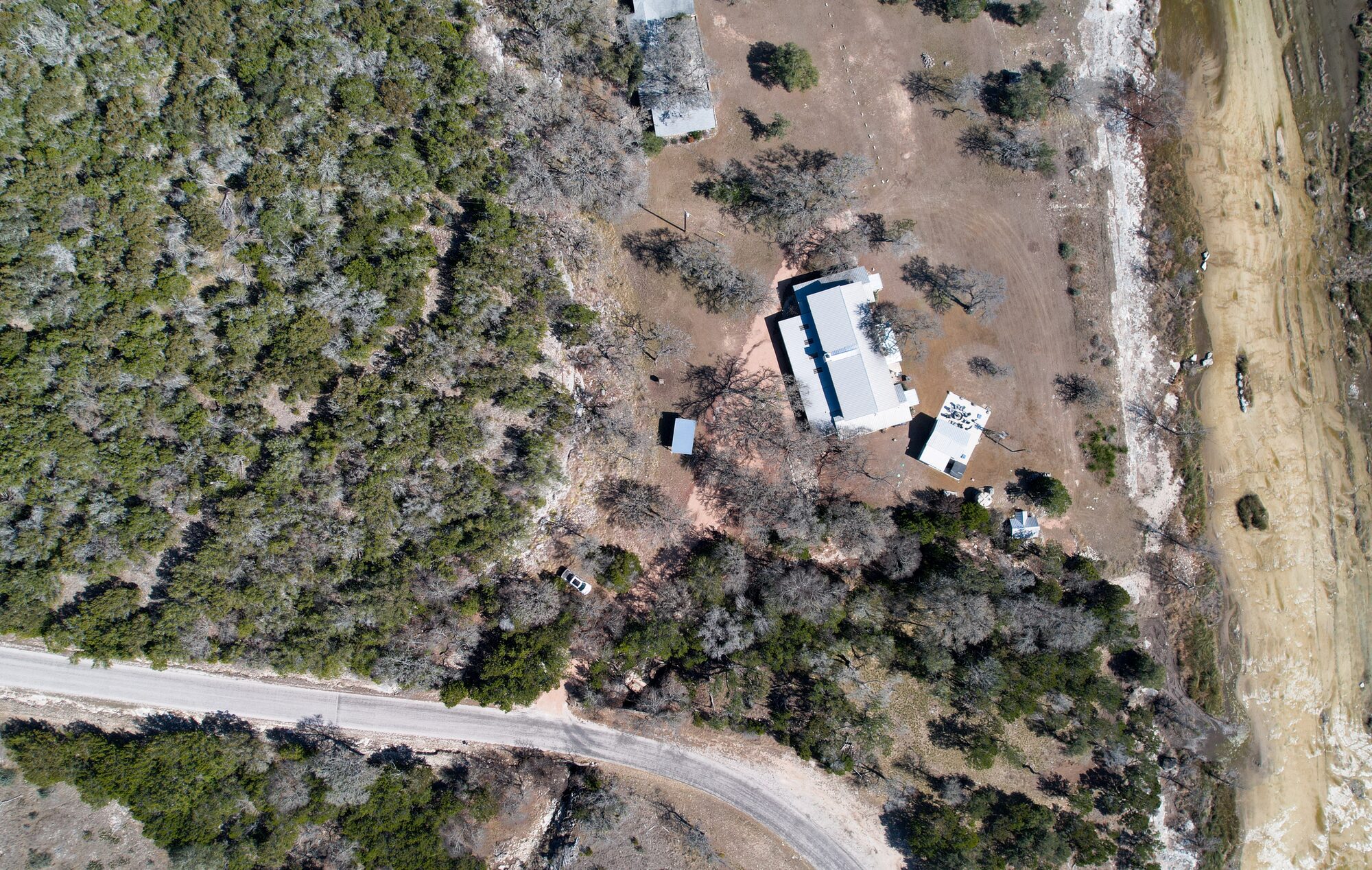 Overhead aerial straight down over 196 Rock Bottom Road showing the metal roofs of the house and the outbuildings, the drive, the oak and cedar cover and the county road along the bottom of the frame