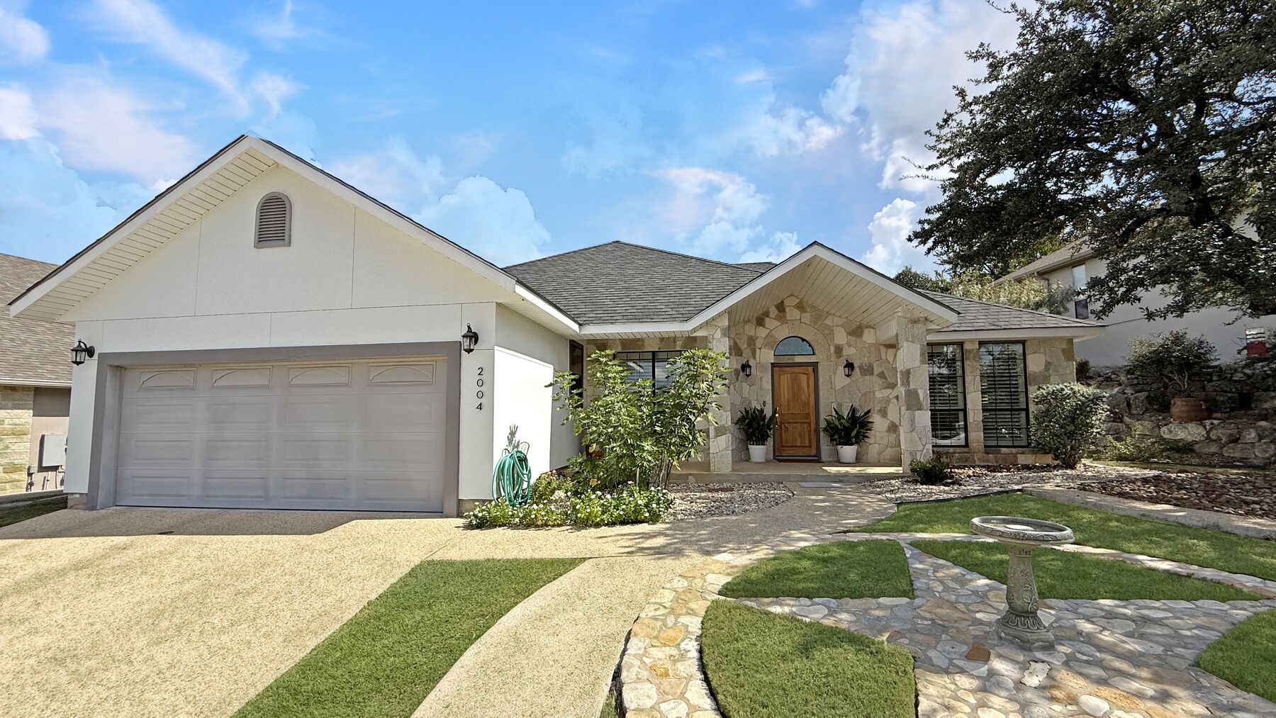 The front of 2004 Athens Ave from the lawn — precast rock and stucco under a composition roof, with a stone walk curving up to the arched front door