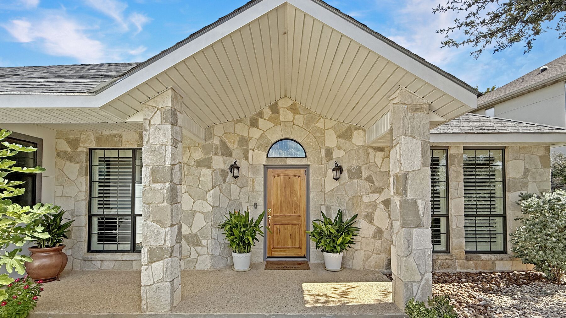 The front entry at 2004 Athens Ave — a stone gable over an arched wood door, with planters either side