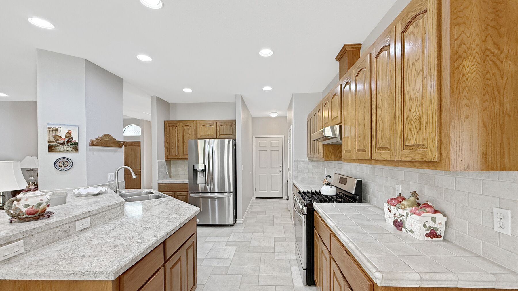 The kitchen at 2004 Athens Ave — wood cabinets, tile counters, a gas range, a stainless refrigerator and a bar at the island