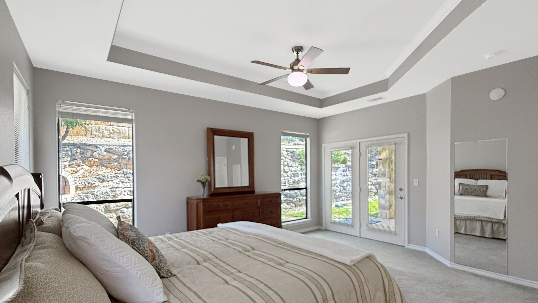 The primary bedroom at 2004 Athens Ave looking toward the back of the house, with a glazed door out to the covered porch and windows onto the stone retaining wall