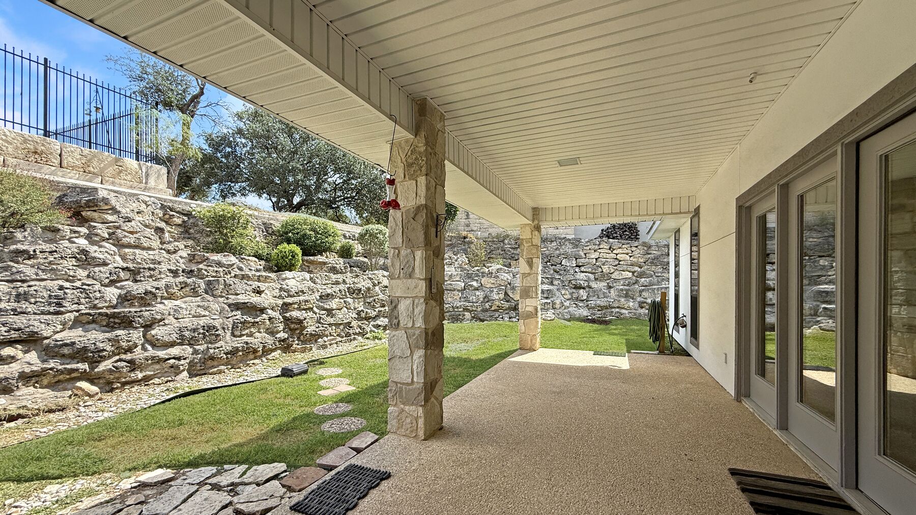 The covered back porch at 2004 Athens Ave running the length of the house, with painted columns, a beadboard ceiling and a stone retaining wall along the lawn