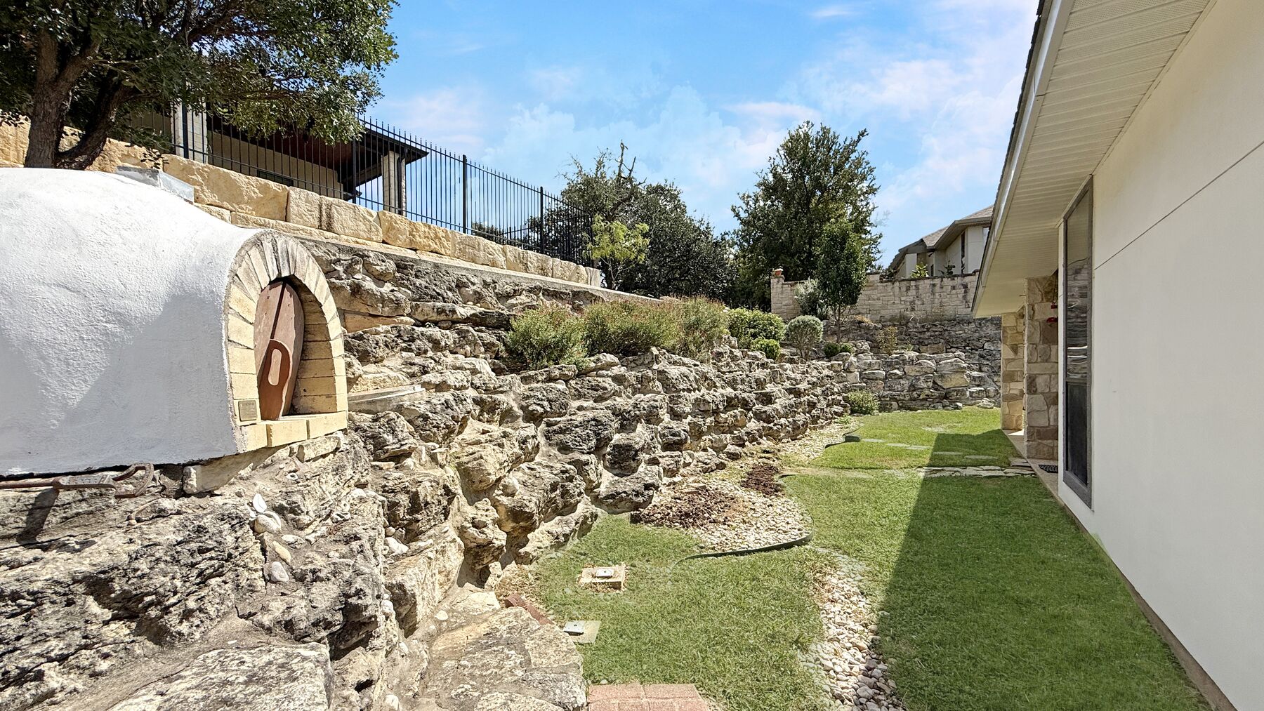 The outdoor pizza oven at 2004 Athens Ave — a domed masonry oven built into the stone retaining wall at the edge of the back lawn