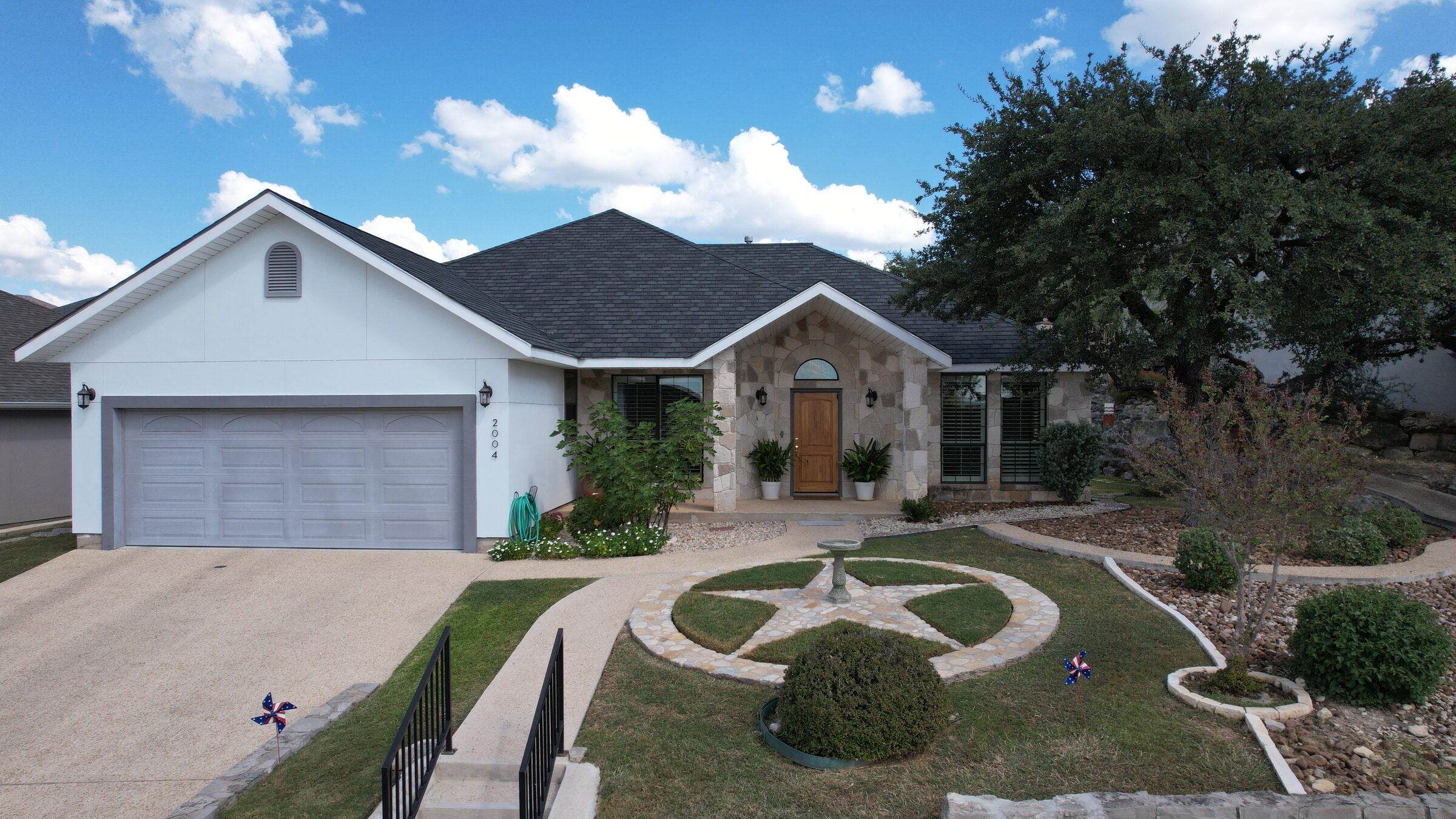 The front of the one-story stone-and-stucco house at 2004 Athens Ave, Kerrville, Texas, with a gabled entry, a two-car garage and a landscaped front lawn