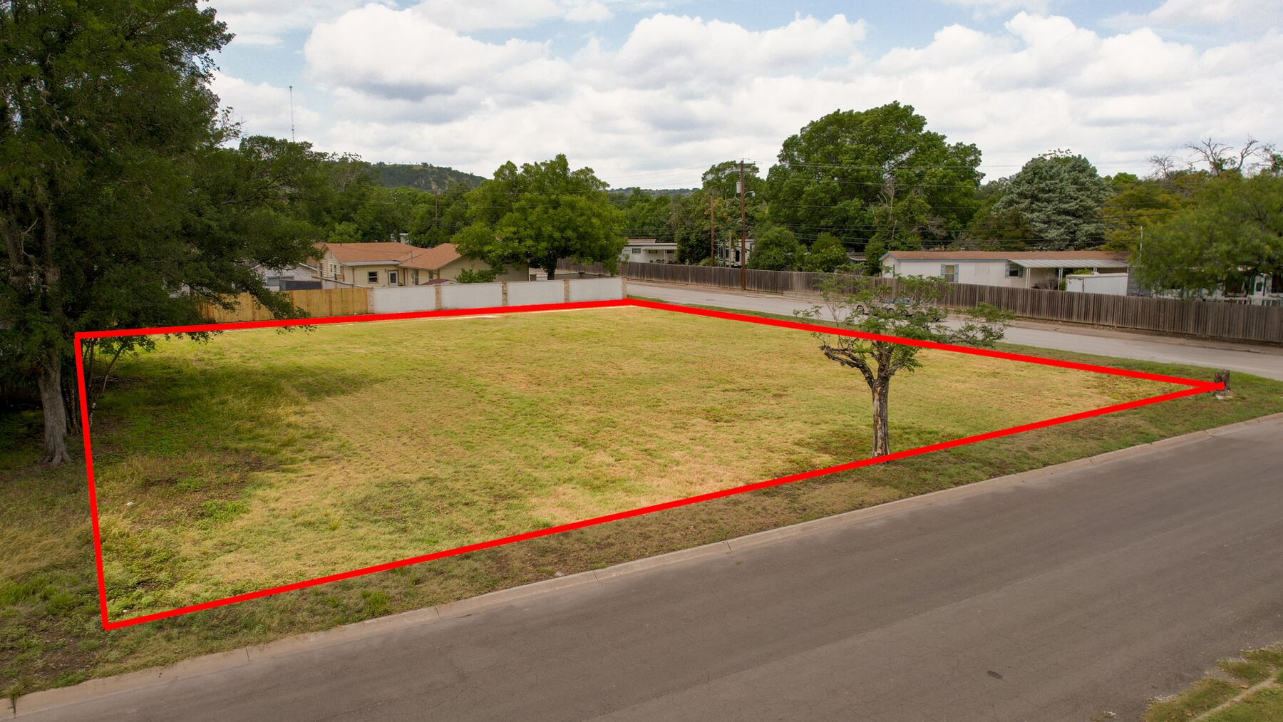 Elevated view of the open ground at 519 Lucille St with the property outline drawn in red, enclosing one continuous area between two paved streets