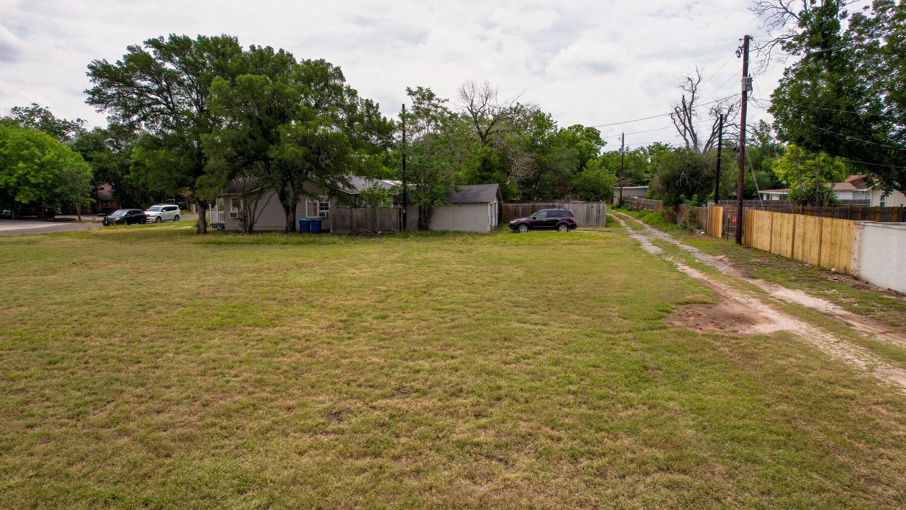 Looking along the side of the property toward a neighbouring house and its outbuildings, with a dirt and gravel track running along the fence line at right. The buildings in this frame stand on adjoining property and are not included in the sale.