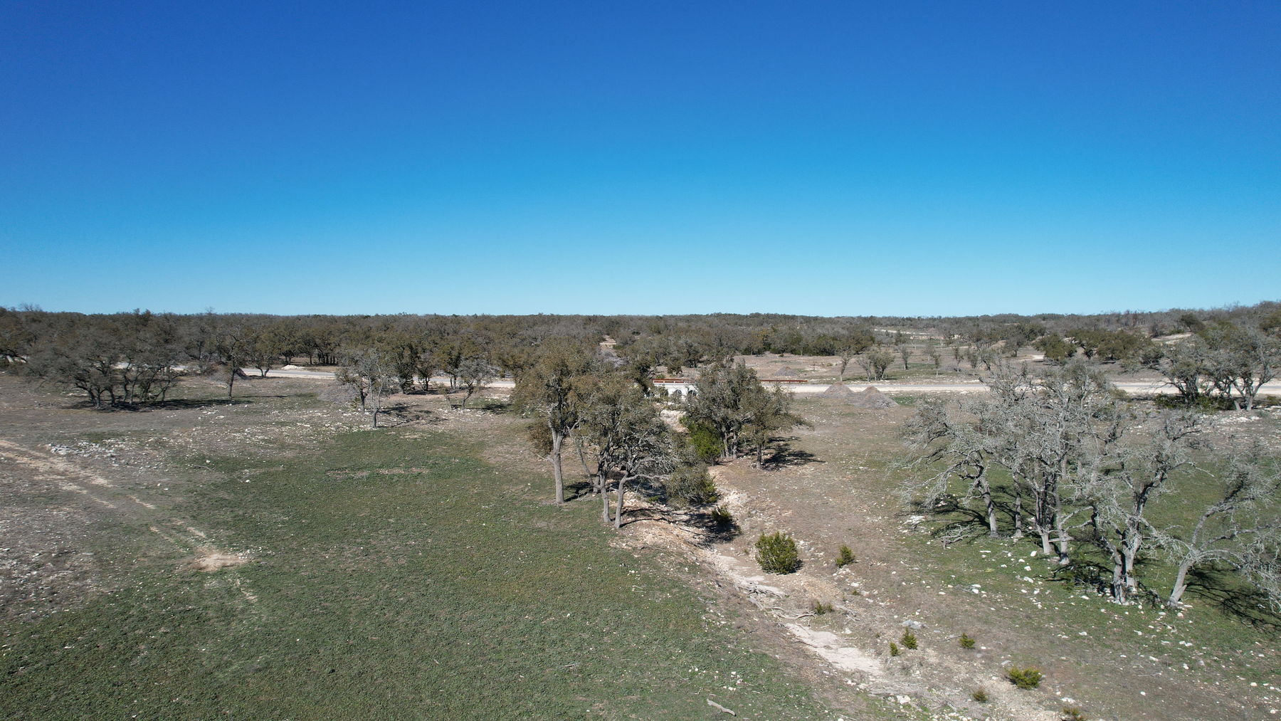 Aerial of winter ground cover across the open portion, with the paved subdivision road running along the far edge