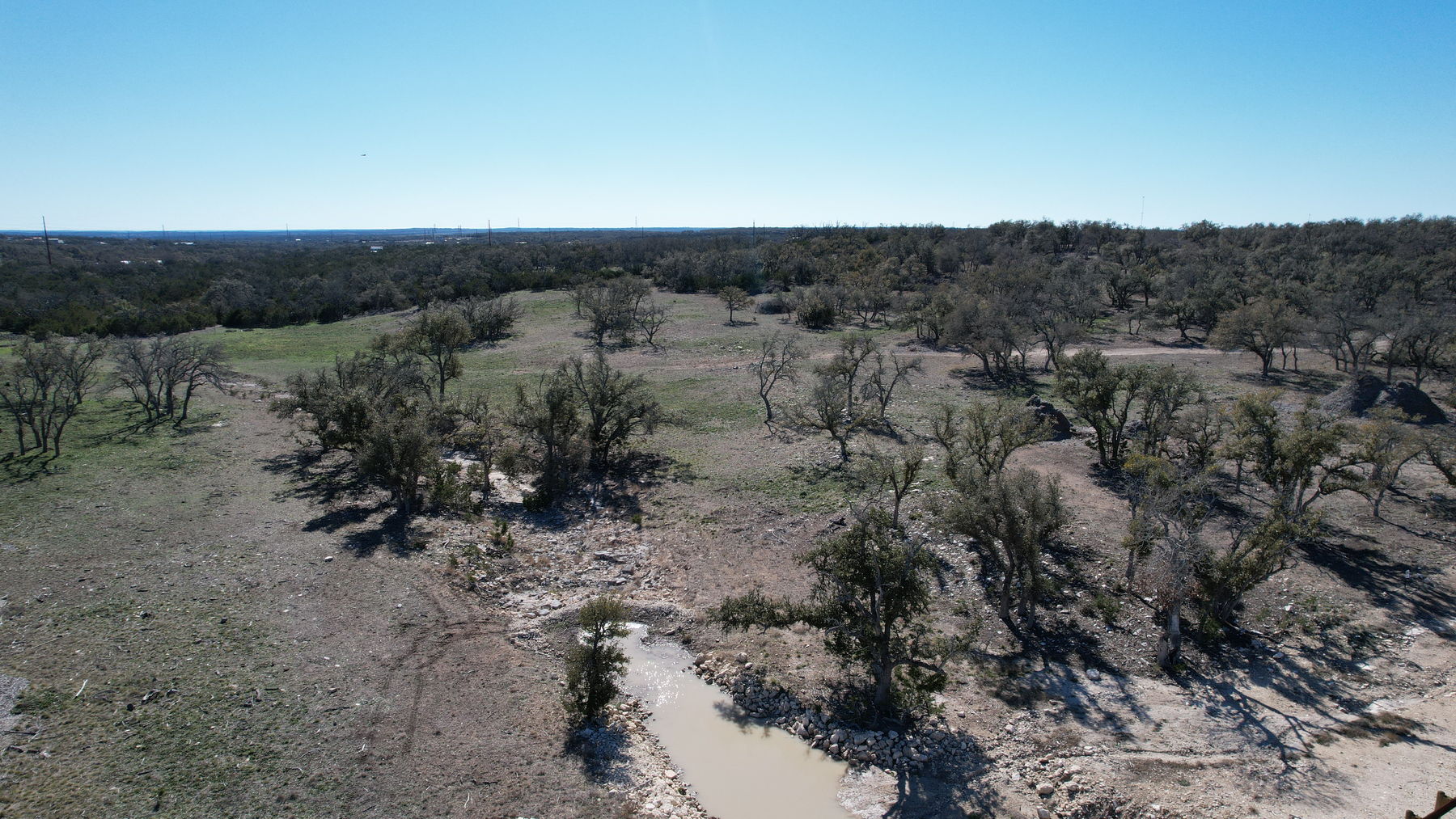 Aerial looking out across the low ground of the property, with the rocky drainage crossing the foreground and Hill Country beyond