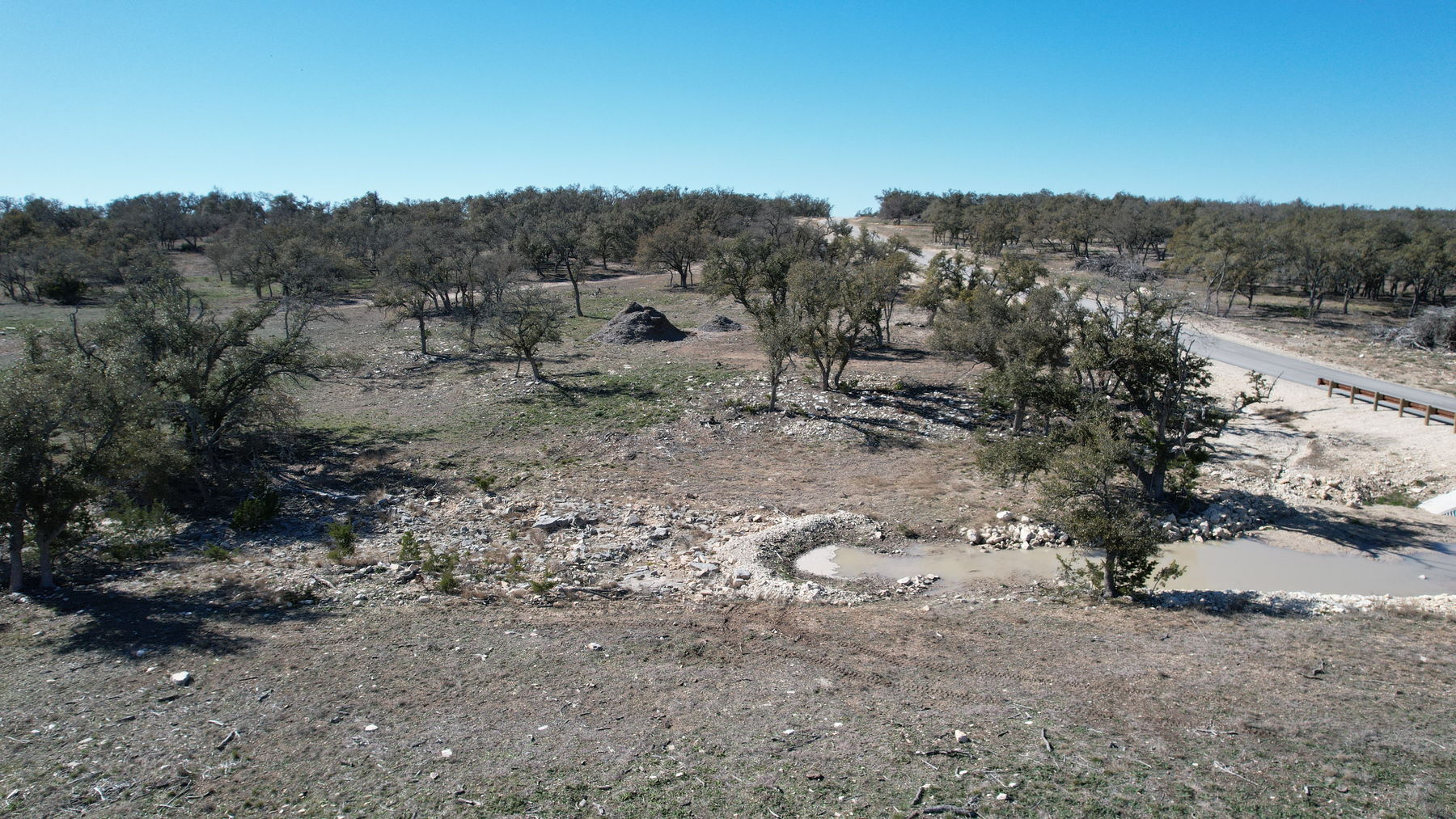 Aerial of a stone-rimmed basin holding shallow standing water below the road crossing