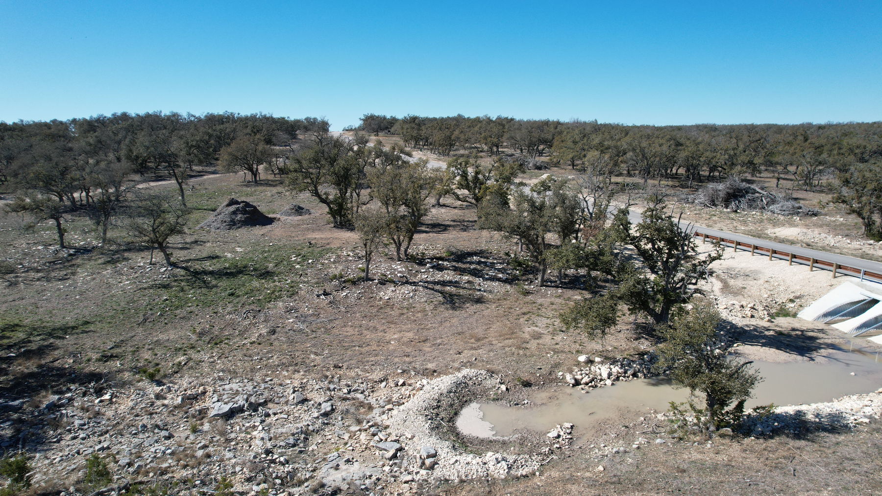 Aerial of the same basin from a second angle, with the concrete apron and guardrail of the subdivision road's culvert at right