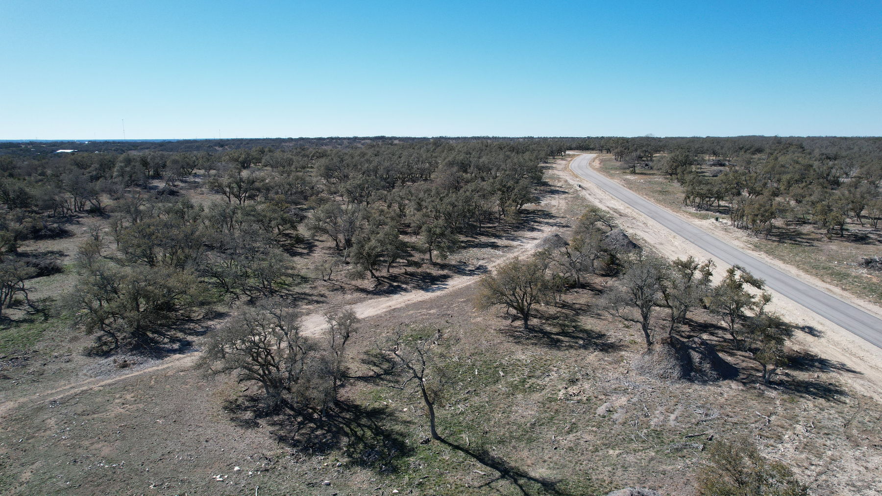 Aerial of a caliche drive cut leaving the paved road at the edge of the tree line